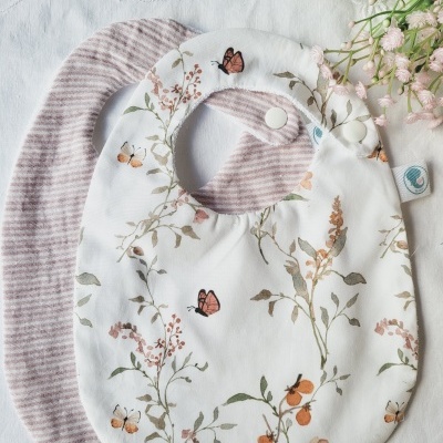 Dois babetes para bebé, um rosa às riscas e outro branco com estampado floral e borboletas