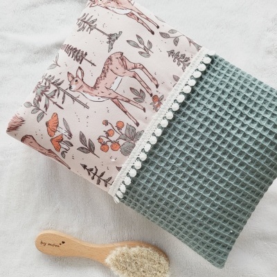 Toalha estampada com veados e folhas combinada com tecido azul texturizado ao lado de escova de cabelo de madeira