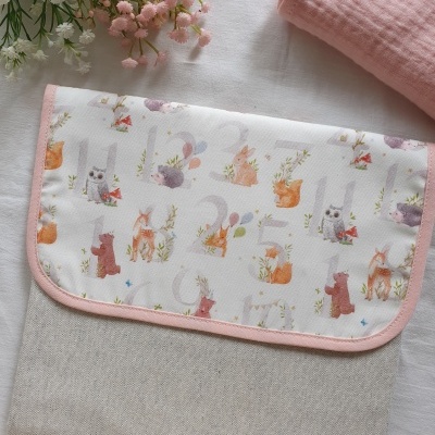 Bolsa de tecido bege com tampa branca estampada com animais e borda rosa