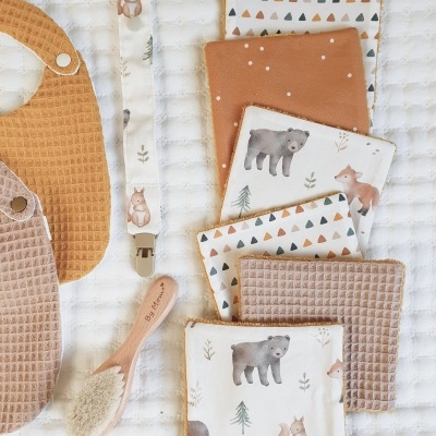 Babete e panos com padrões de animais e triângulos e uma escova de cabelo em fundo branco texturizado