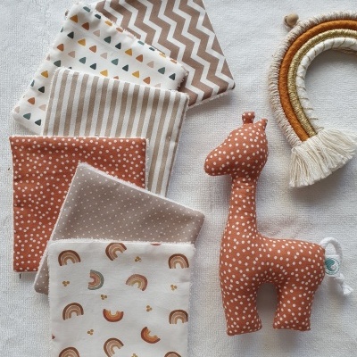 Panos de tecido com padrões variados e brinquedo de girafa de peluche castanha, com arco decorativo de corda