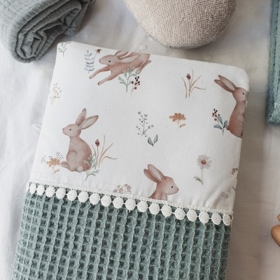 Toalha verde com padrão de coelhos castanhos e faixa de pompons brancos