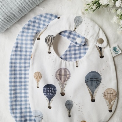 Dois babetes para bebé um com padrão de balões e outro xadrez azul claro e branco