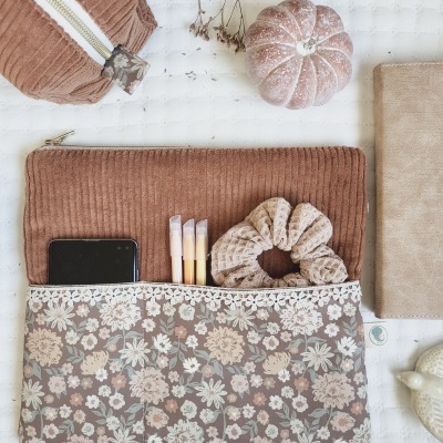 Carteira e necessaire de tecido castanho com padrão floral e acessórios organizados sobre superfície branca
