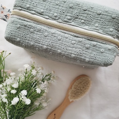 Necessaire de tecido cinza com fecho zipper, escova de madeira e flores brancas