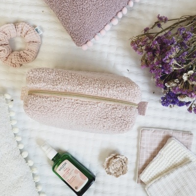 Necessaire rosa felpuda com spray facial e produtos de tecido sobre cama branca textural