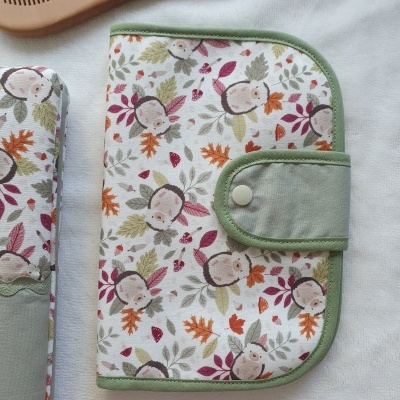 Carteira ou estojo com padrão infantil de folhas e rostos, botão de pressão e bordas verdes