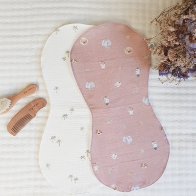 Dois babetes infantis em tecidos estampados, pente e escova de madeira, flores secas sobre fundo branco texturizado.