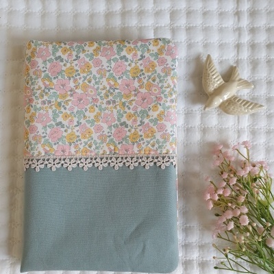 Caderno com capa floral e azul sobre tecido branco com flores e pássaro em cerâmica ao lado