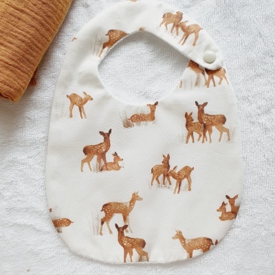 Babete para bebé branco com veados castanhos sobre toalha branca