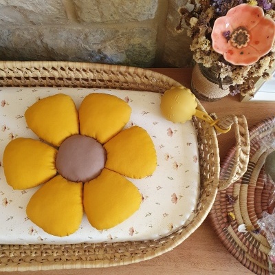 Almofada flor amarela em colchão floral dentro de cesta de verga com flores secas e vaso ao lado.