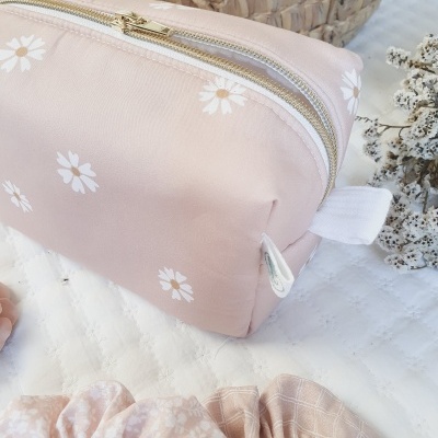 Necessaire rosa claro com flores brancas e fecho dourado com duas molas de cabelo em fundo branco