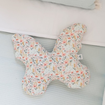 Almofada em forma de borboleta com padrão floral colorido sobre cama azul clara e branca