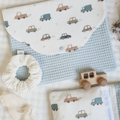 Produtos para bebé: mala, manta, scrunchie e brinquedo de madeira com padrão de carros em tecido azul e branco