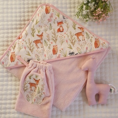 Conjunto de toalha rosa com capuz estampado, saco e brinquedo de girafa em fundo branco texturado.