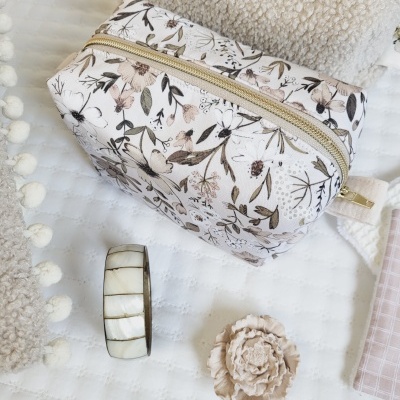 Estojo floral beige com fecho dourado e pulseira branca em superfície branca texturizada