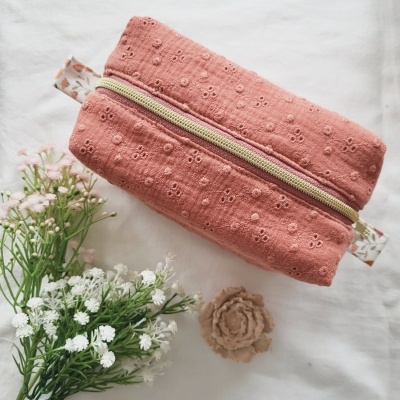 Necessaire rosa bordada com fecho de correr e alças florais sobre fundo branco com flores