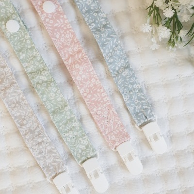 Cinco fitas de tecido floral coloridas com clipes brancos sobre tecido branco acolchoado