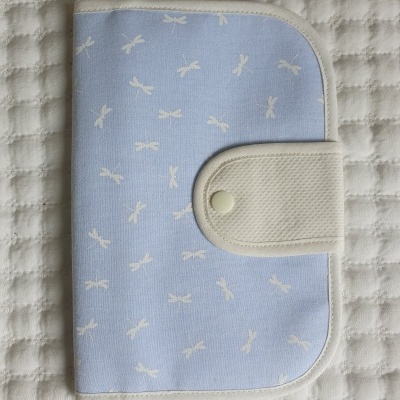 capa ou estojo azul com laços brancos e fecho branco sobre tecido branco acolchoado