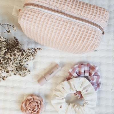 Estojo rosa claro com scrunchies, batom e flor sobre superfície branca texturada