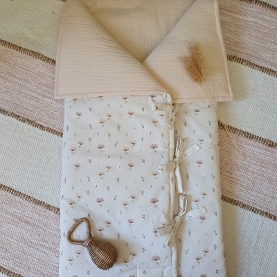 Saco de dormir para bebé com padrão floral e capuz creme sobre superfície texturada bege e rosa