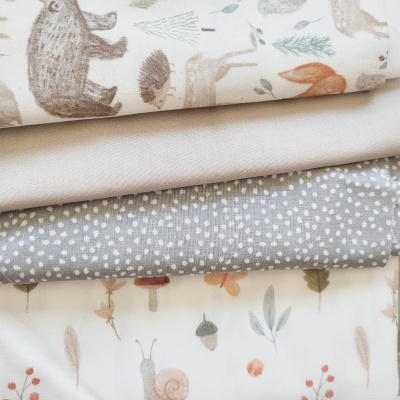 Cinco tecidos dobrados com diferentes padrões, incluindo animais da floresta, bolinhas, estrelas e ilustrações naturais.