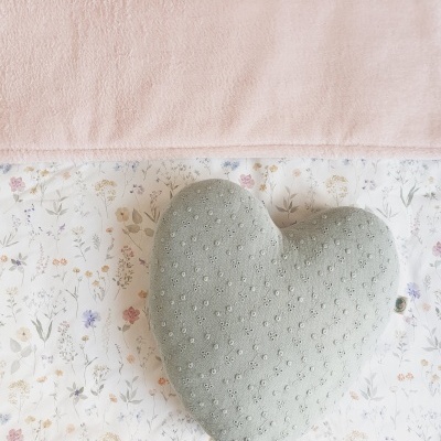 Travesseiro em forma de coração verde-acinzentado com padrão bordado sobre tecido floral e rosa claro