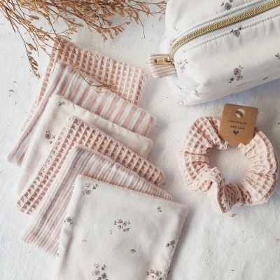 Toalhitas de tecido floral e listradas com estojo e elástico de cabelo rosa em tecido, sobre superfície branca.