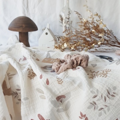 Tecido branco com padrões de folhas e pássaros em tons terra com elástico de cabelo cor de malva, decoração em fundo.