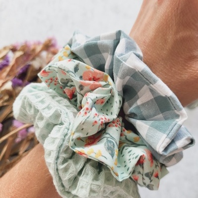Três scrunchies de tecido com diferentes padrões e cores no pulso.