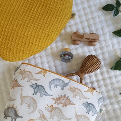 Saco de tecido com padrão de dinossauros e brinquedos sobre superfície acolchoada branca