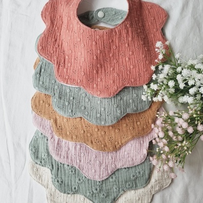 Seis babetes de bebé coloridos em tecido bordado, arranjados em camadas com flores ao lado