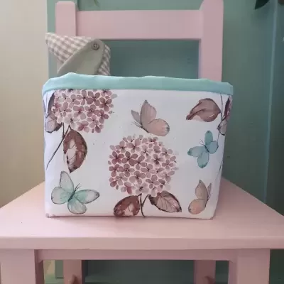 Cesto de tecido floral com borboletas numa cadeira rosa