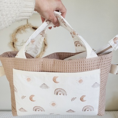 Bolsa de bebé bege com alças estampadas e bolsos frontais decorados com luas, sóis e arco-íris em tons pastel