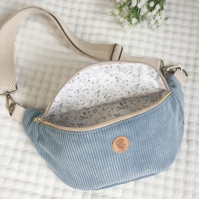 Bolsa pochete azul claro com interior floral e alça bege sobre tecido branco