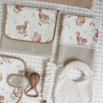 Conjunto de acessórios para bebé com padrão de esquilos em bege e branco sobre tecido texturado
