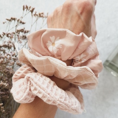 Três scrunchies rosa com padrões florais, quadriculados e textura de malha no pulso