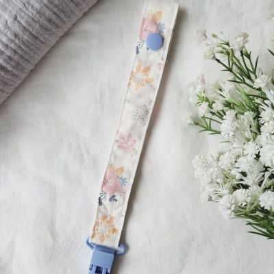 Fita floral com clip azul sobre superfície branca, ao lado de toalha cinza e flores brancas