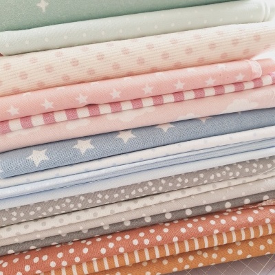 Pilha de tecidos variados com padrões de estrelas, bolinhas e riscas em cores pastel