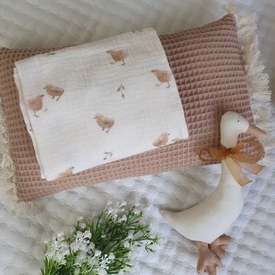 Almofada castanha com manta de pintainhos e brinquedo pato em fundo branco