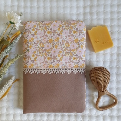 Capa de tecido floral e castanho com renda, sabonete amarelo SAVON e massageador de madeira sobre tecido branco acolchoado.