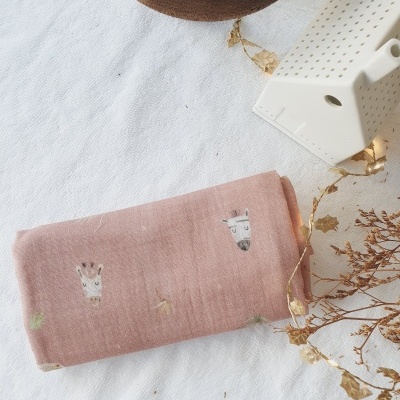 tecido rosa com desenhos de animais, peça branca decorativa em forma de casa, objeto castanho e ramos secos