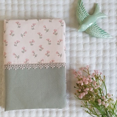 Capa de tecido floral com renda e decoração de pássaro verde sobre superfície branca