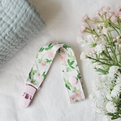 Tira de tecido floral com fecho plástico rosa sobre tecido branco próximo de flores e tecido cinza