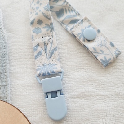 Presilha para chupeta azul com padrão floral sobre fundo branco