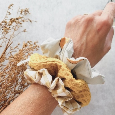 Três scrunchies de tecido coloridos no pulso de uma mão