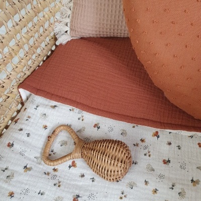 Berço com tecido floral, almofadas terracota e bege, e brinquedo em rattan trançado