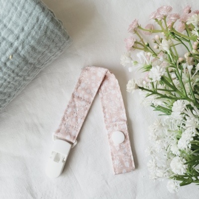 Prendedor de chupeta cor-de-rosa com clip branco sobre tecido branco e flores