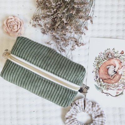 Necessaire verde canelado com elástico xadrez, flores secas e cartão com ilustração de animais.