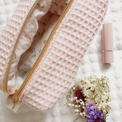 Nécessaire rosa claro com fecho dourado e interior estampado ao lado de batom rosa e flores secas